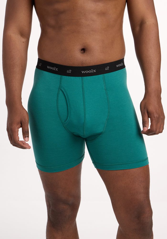 A man models the Woolx Reaction Boxer Briefs in Woodland Mini Stripe, featuring a black "woolx" waistband. He stands against a white background with his head out of frame. | Trell is 6’2”, wearing a size M