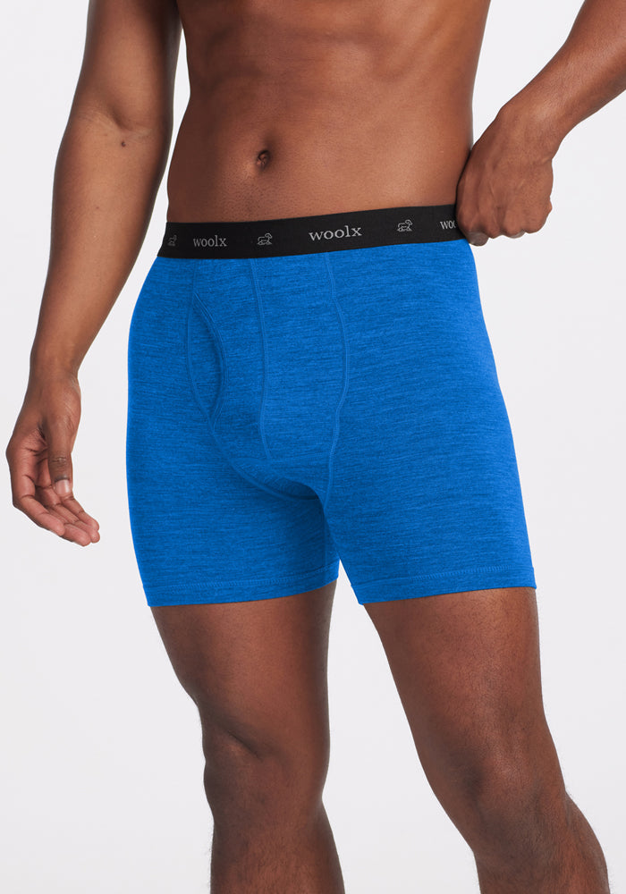 A person wearing Woolx Reaction Boxer Briefs in Glacial Blue, featuring a black waistband with the Woolx logo, stands against a plain white background. | Trell is 6’2”, wearing a size M