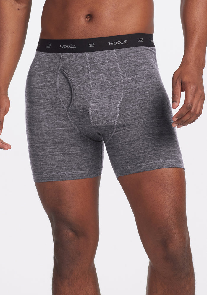 A person is wearing Graphite Heather Reaction Boxer Briefs by Woolx, featuring a black waistband with "woolx" text. The image highlights the performance boxer design on their lower torso and upper thighs against a plain background.