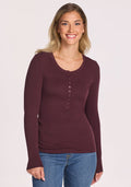 A woman with long blonde hair smiles while wearing the Woolx Reese Ribbed Henley in Chocolate Fig and blue jeans against a plain light background. | Ariana is 5'11", wearing a size S