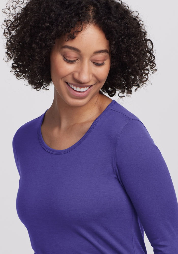 Smiling woman with curly hair in Woolx Remi Long Sleeve T-Shirt in Berry Indigo, looking down.