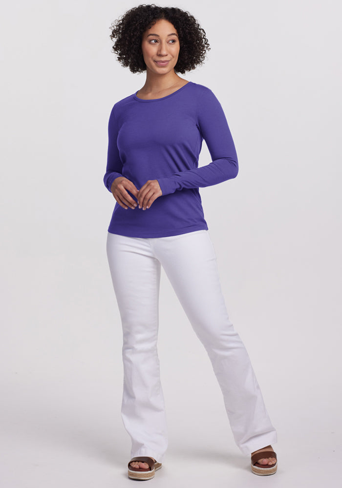 Woman with curly hair wearing the Woolx Remi Long Sleeve T-Shirt in Berry Indigo and white jeans, smiling.