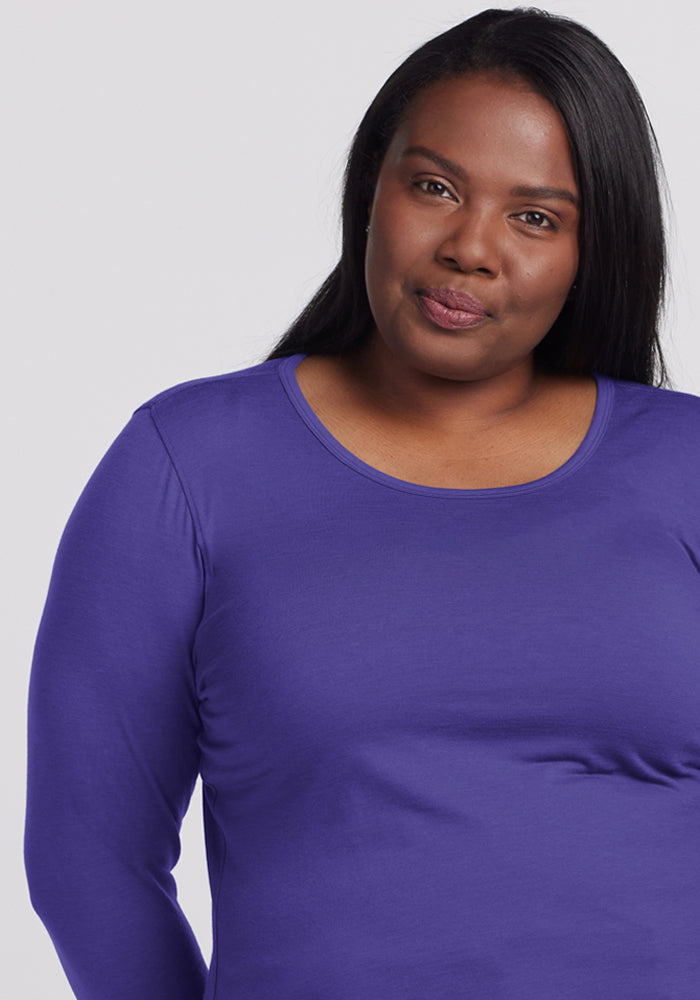 A woman with long dark hair wears the Woolx Remi Long Sleeve T-Shirt in Berry Indigo, standing against a light background.