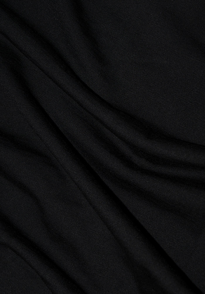 A close-up of the Remi Long Sleeve T-Shirt in Black by Woolx showcases its Merino wool fabric. The subtle folds and wrinkles create a soft, flowing texture, highlighting the moisture-wicking material's smooth and slightly reflective surface, with gentle shadows adding depth.