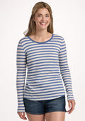 A smiling woman with long, light brown hair wears the Woolx Remi Long Sleeve T-Shirt in Blue Sand Stripe and denim shorts, standing against a plain white background. | Ariana is 5'11", wearing a size S