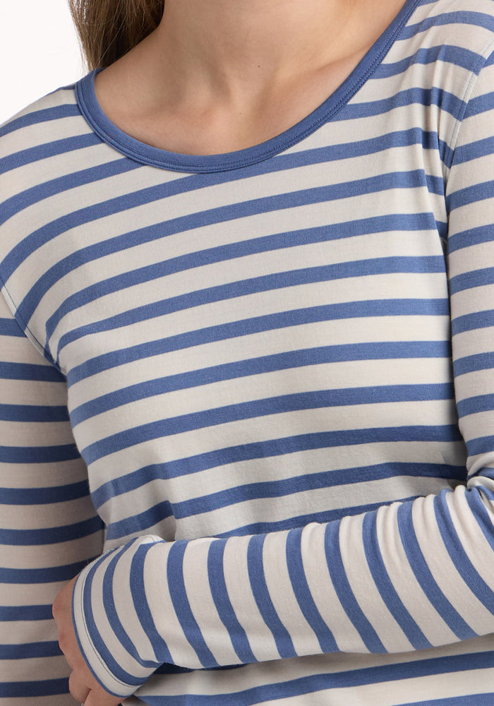 A person wears the Woolx Remi Long Sleeve T-Shirt in Blue Sand Stripe, shown from shoulders to waist with one arm crossed over their body.