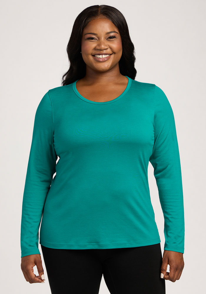 A woman smiles in a Woolx Remi Long Sleeve T-Shirt - Cabana Crush and black pants against a light background. | Sapphire is 5’8”, wearing a size XL