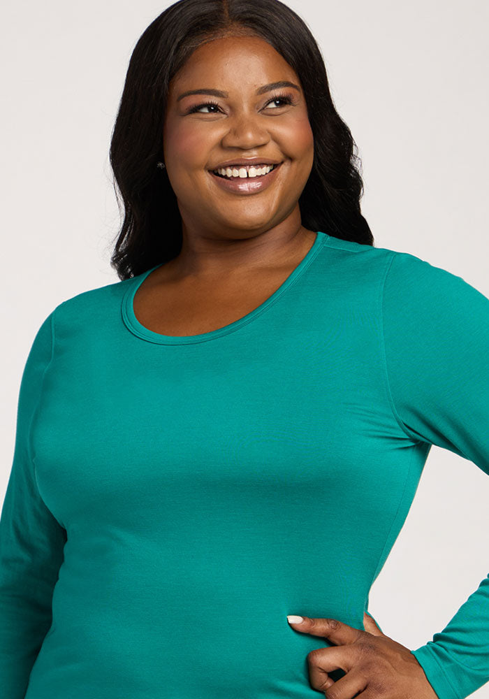 Smiling woman in a Woolx Remi Long Sleeve T-Shirt—Cabana Crush stands with one hand on her hip against a light background.