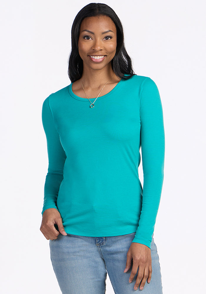 Woman wears the Woolx Remi Long Sleeve T-Shirt in Cool Jade and blue jeans, smiling against a light background.