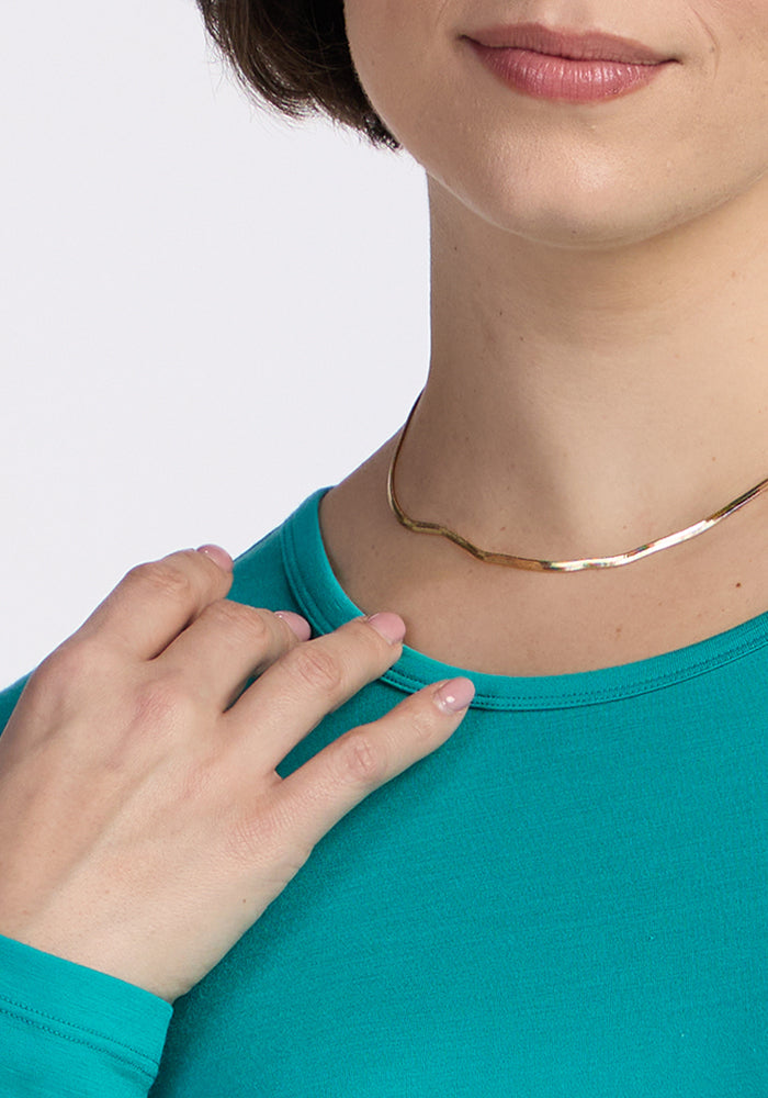 A person in a Woolx Remi Long Sleeve T-Shirt in Cool Jade touches their collar, showing a gold necklace and part of their face.