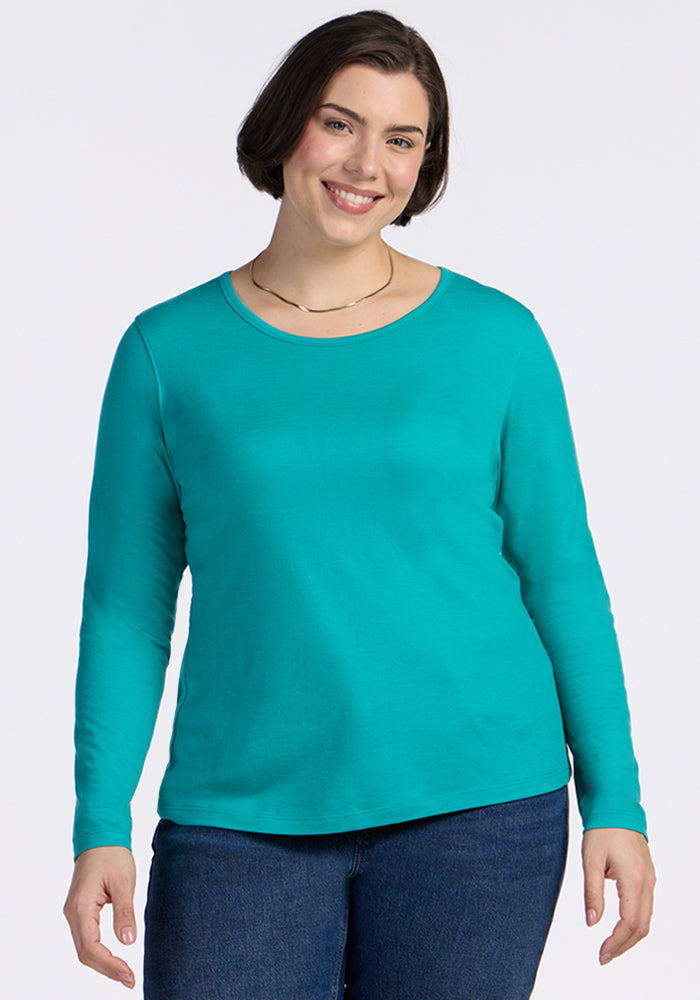 Smiling woman with short brown hair in a Woolx Remi Long Sleeve T-Shirt in Cool Jade and blue jeans.