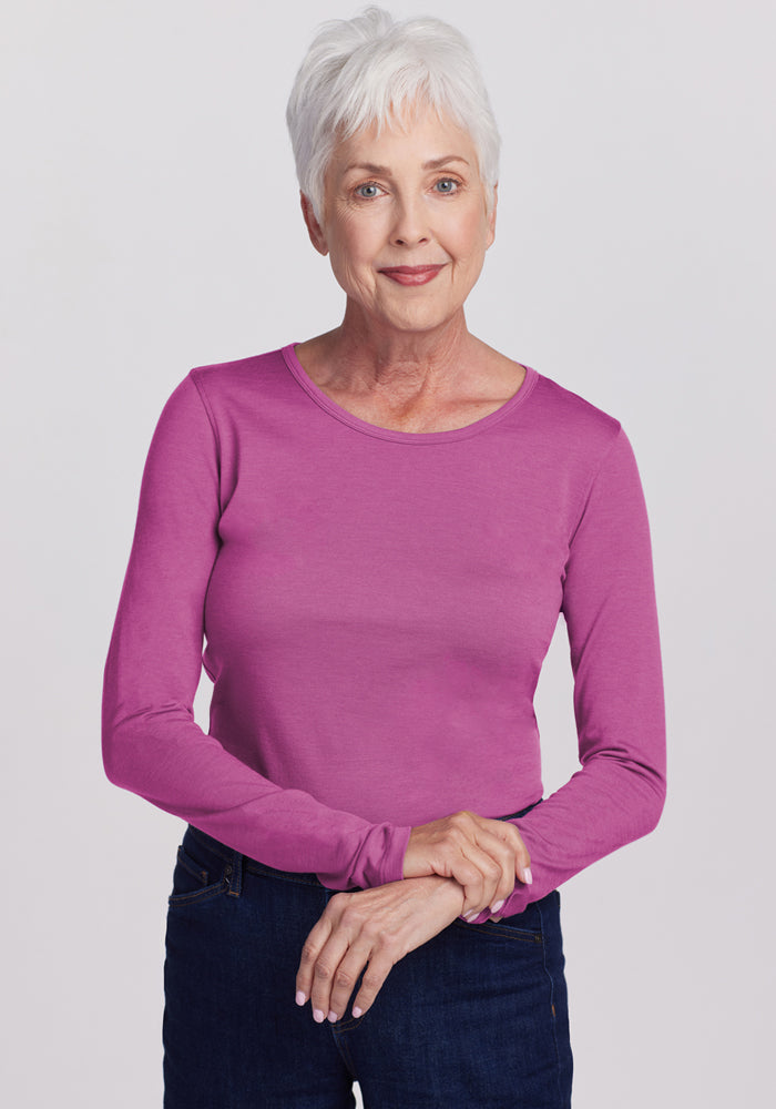 Smiling older woman in a Woolx Remi Long Sleeve T-Shirt in Purple Wine and dark jeans, against a plain background.