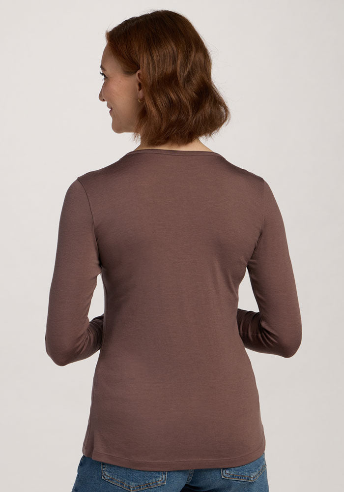 A woman in the Woolx Remi Long Sleeve T-Shirt in Peppercorn and jeans stands with her back to the camera, looking aside.