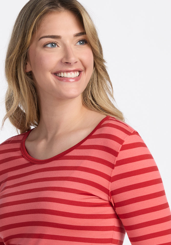 A smiling woman with light brown hair wears the Woolx Remi Long Sleeve T-Shirt in Wildberry Stripe, an odor-resistant travel top, as she looks slightly to the side against a plain light background.