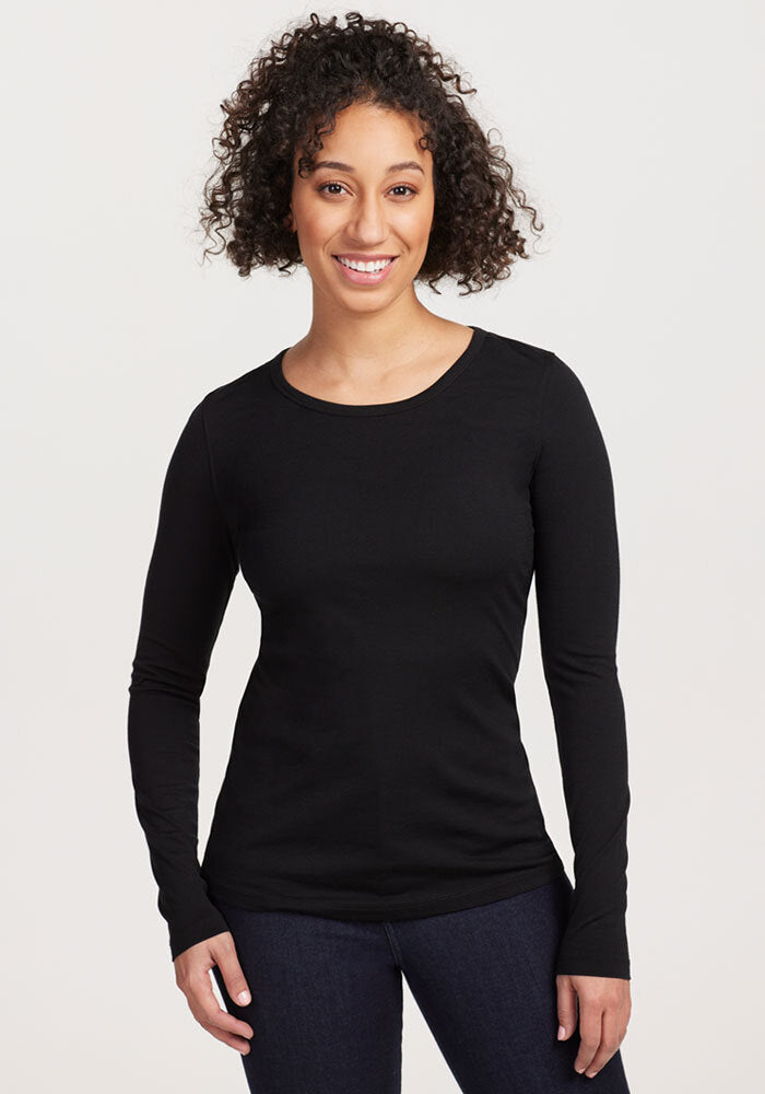 Woman with curly hair smiles in a Woolx Remi Long Sleeve T-Shirt - Black, paired with dark jeans, on a light background. | Tori is 5'7", wearing a size S