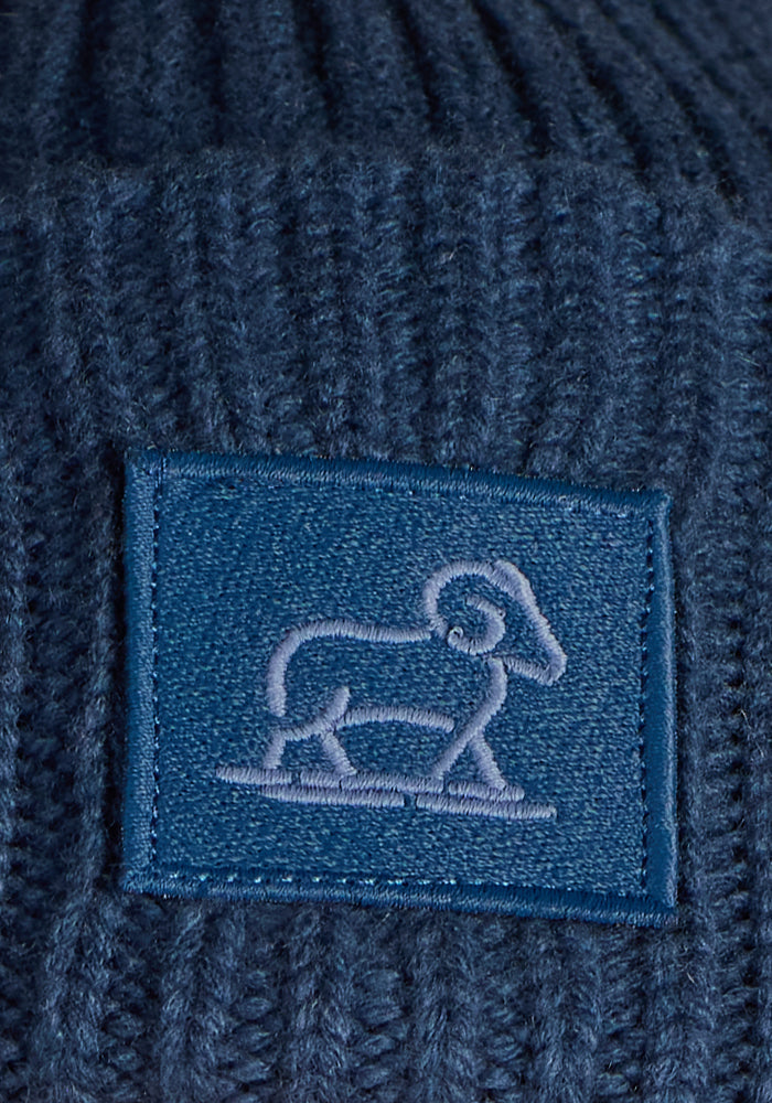 A close-up of the Woolx Ria Chunky Beanie - Starry Night, featuring a ribbed blue knit design with a rectangular patch embroidered with a sheep outline—perfect for cozy winter wear.