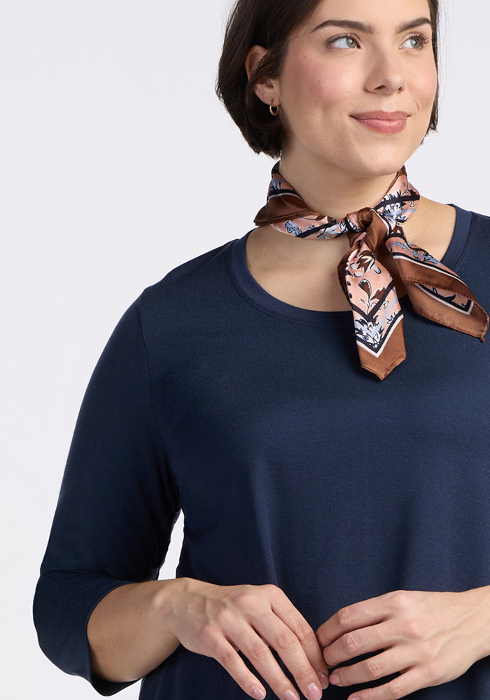 A woman in the Woolx Rissa A Line Dress in Deep Navy, paired with a patterned brown scarf and a gentle smile, offers chic fall-winter layering inspiration against a plain light background.