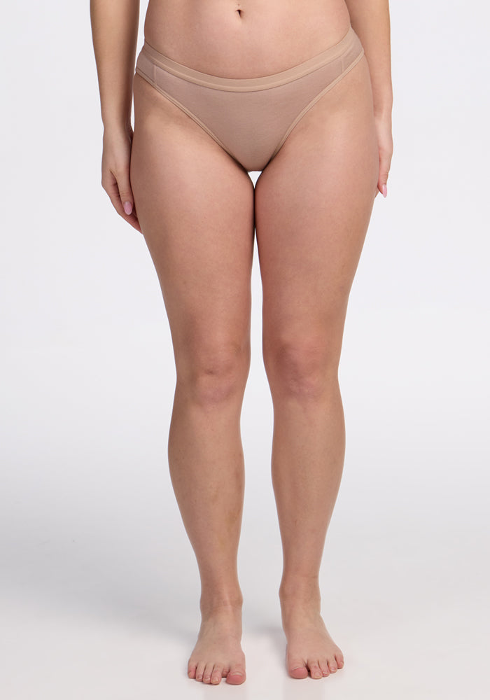 A woman stands barefoot against a white background, wearing Woolx Roxie Bikini Underwear in Morning Latte. The image highlights the comfort and fit of this high-quality Merino wool underwear, shown from the shoulders down.