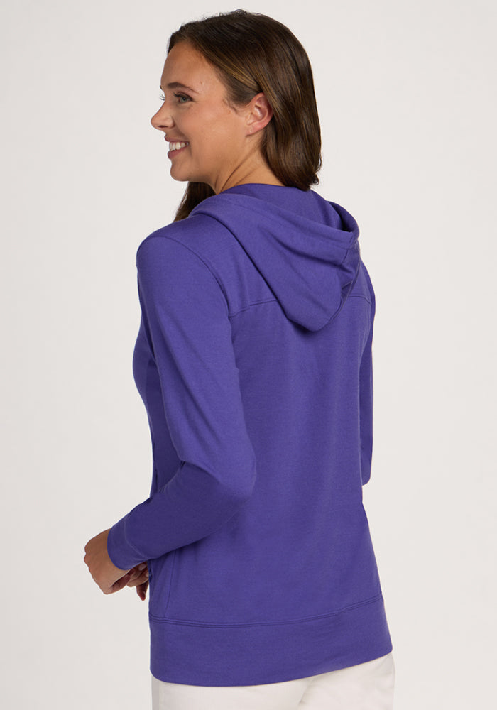 Woman smiling, shown from the back in a studio, wearing Woolx Ryann Hoodie - Berry Indigo and white pants.