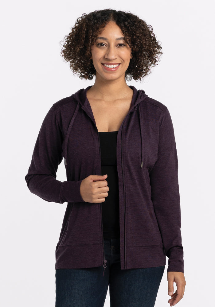 Woman smiling in the Woolx Ryann Hoodie • Final Sale - Deep Plum over a black top and blue jeans, on a white background.