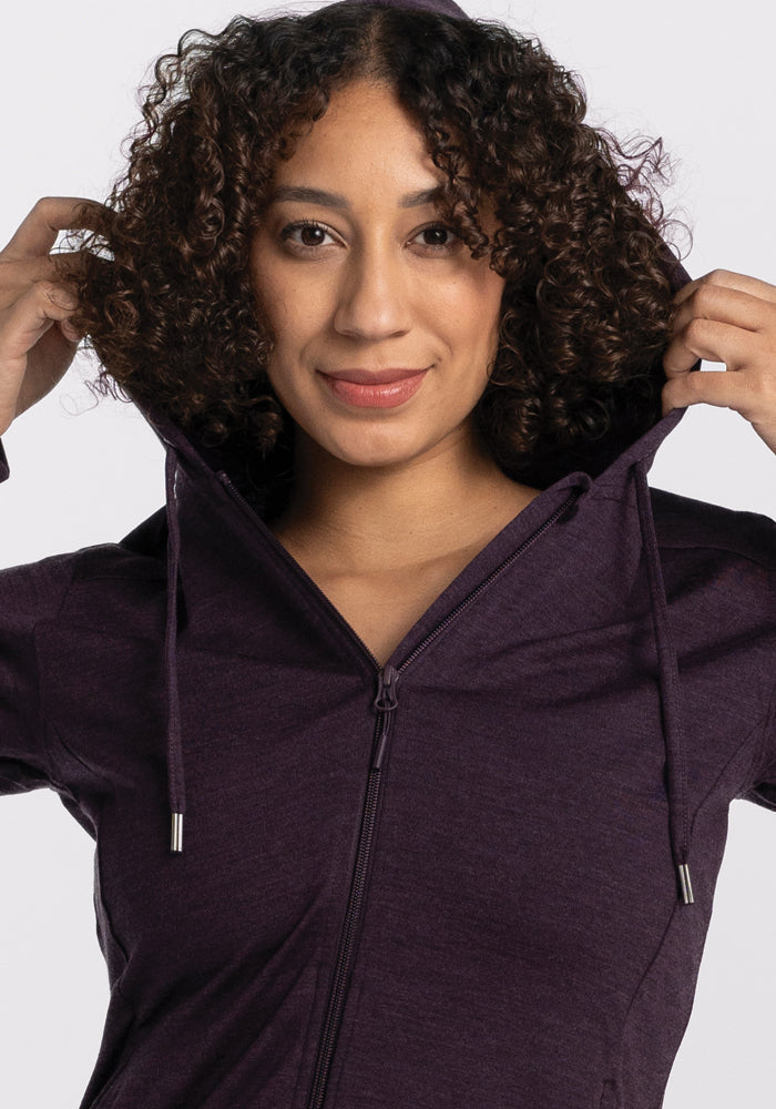 Woman with curly hair in the Woolx Ryann Hoodie • Final Sale - Deep Plum, holding the hood and smiling softly.