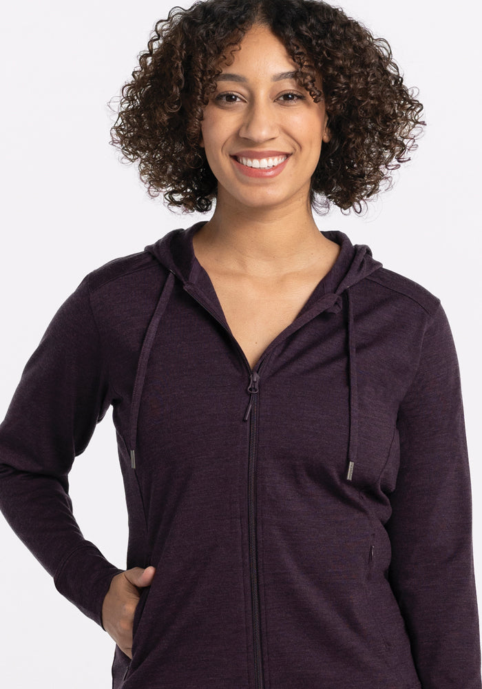A smiling woman with curly hair wears the Woolx Ryann Hoodie in Deep Plum, with one hand in her pocket.