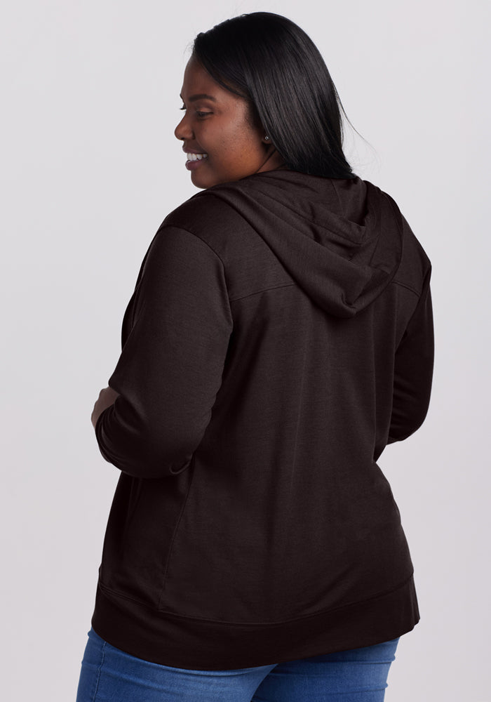 Woman smiling, wearing the Woolx Ryann Hoodie in French Roast and blue jeans, facing away on a plain background.