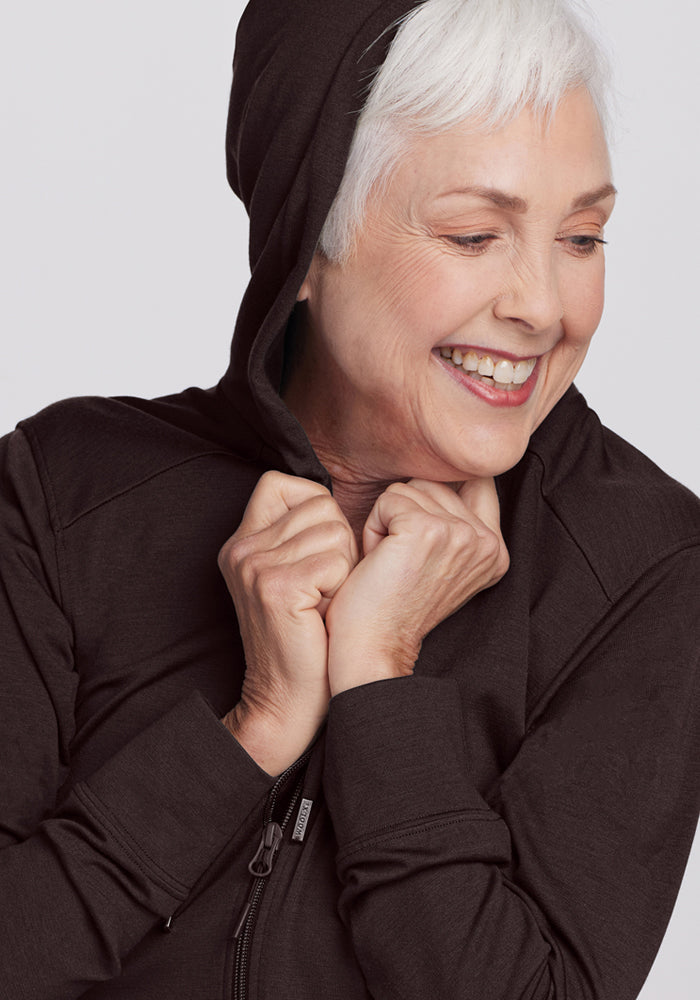 Smiling older woman with short white hair wears the Woolx Ryann Hoodie • Final Sale - French Roast, holding the hood.