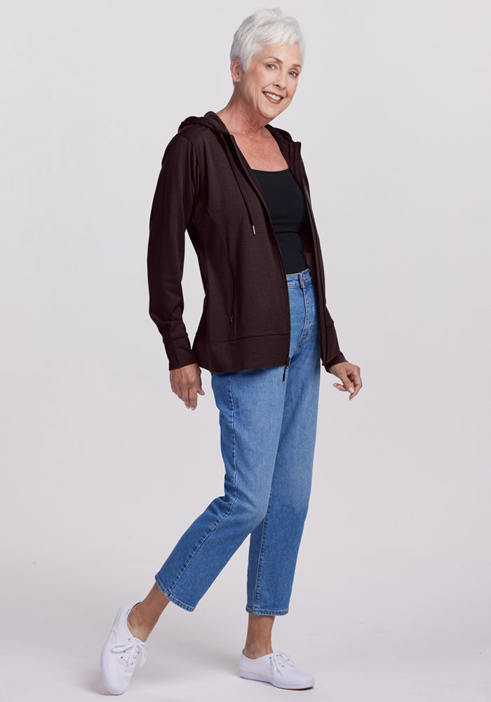 Older woman smiling and walking in a Woolx Ryann Hoodie in French Roast, blue jeans, and white sneakers.