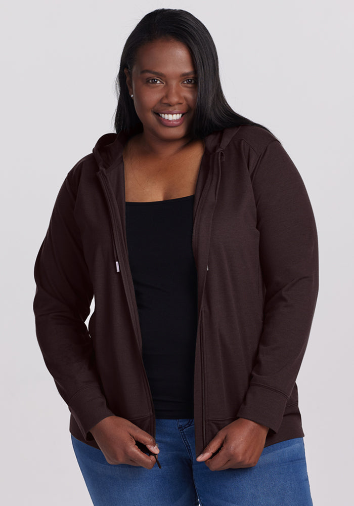 Smiling woman wears the Woolx Ryann Hoodie in French Roast, black top, and blue jeans against a light background.