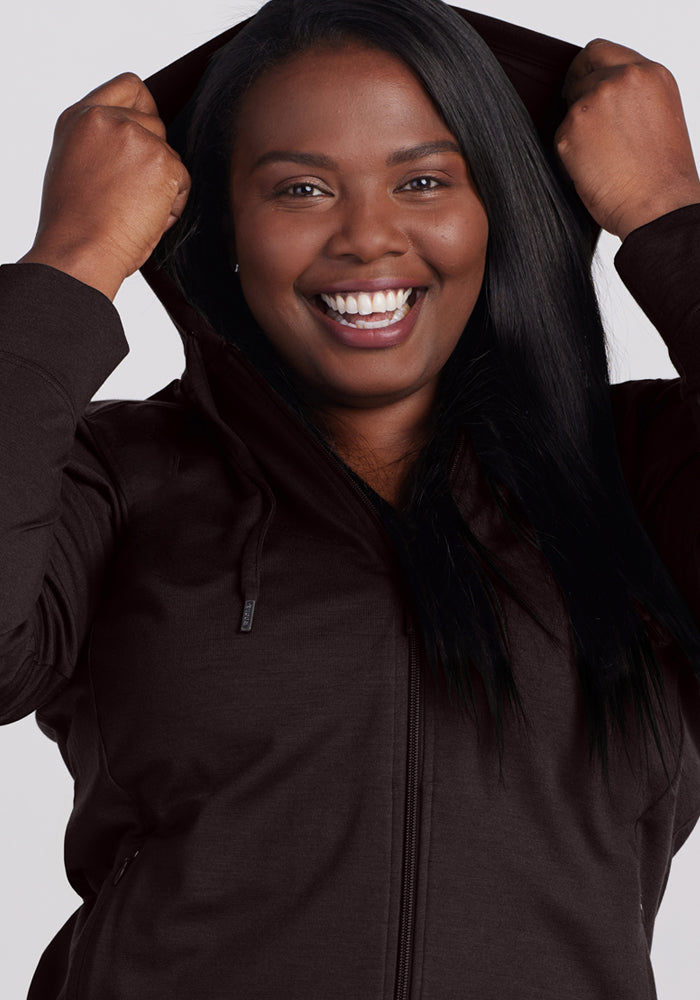 Smiling woman in a Woolx Ryann Hoodie • Final Sale - French Roast, holds up the hood facing the camera.