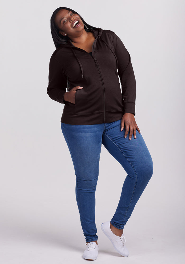 Woman smiling in a Woolx Ryann Hoodie • Final Sale - French Roast, blue jeans, and white shoes against a plain background.