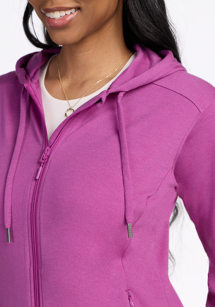 Smiling woman wears the Woolx Ryann Hoodie in Purple Wine over a white top with a gold necklace—a travel essential.