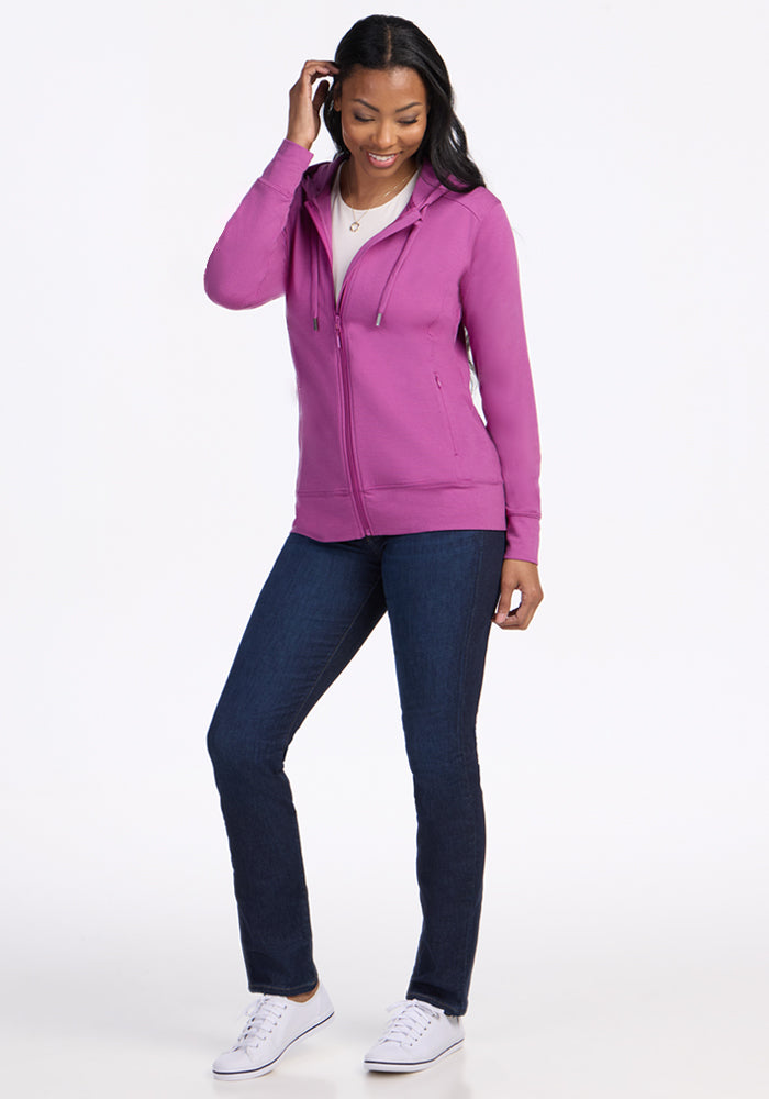 Woman smiling in a Woolx Ryann Hoodie in Purple Wine, paired with jeans and white sneakers on a plain background.