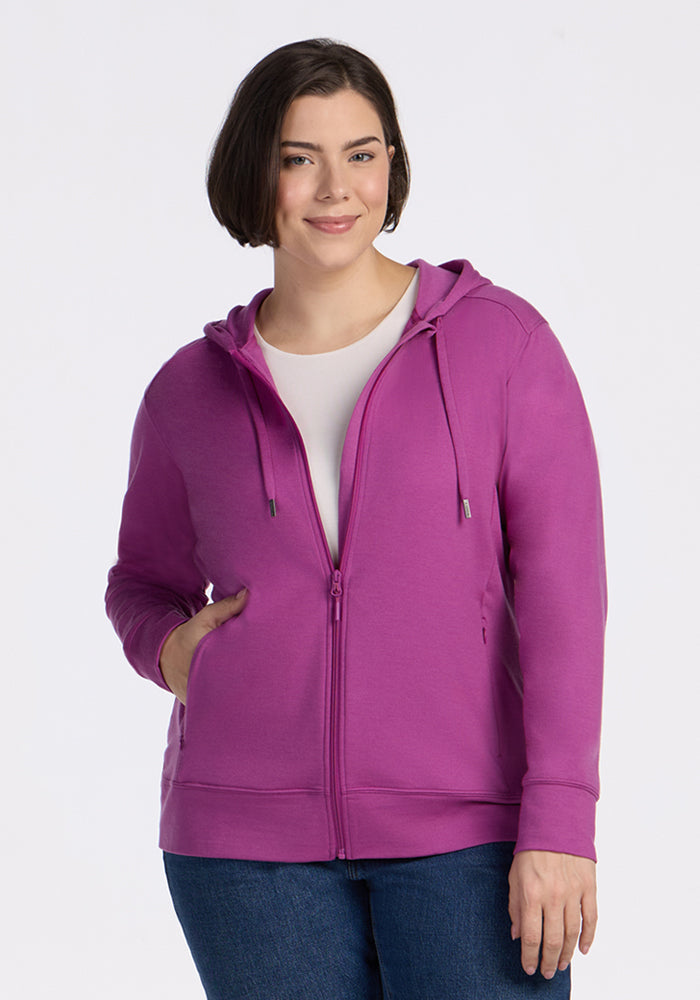 A woman in a Woolx Ryann Hoodie in Purple Wine and jeans smiles at the camera against a white background.
