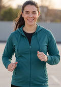A smiling woman jogs outdoors in the Woolx Ryann Hoodie • Final Sale - Tidepool on a sunny day.