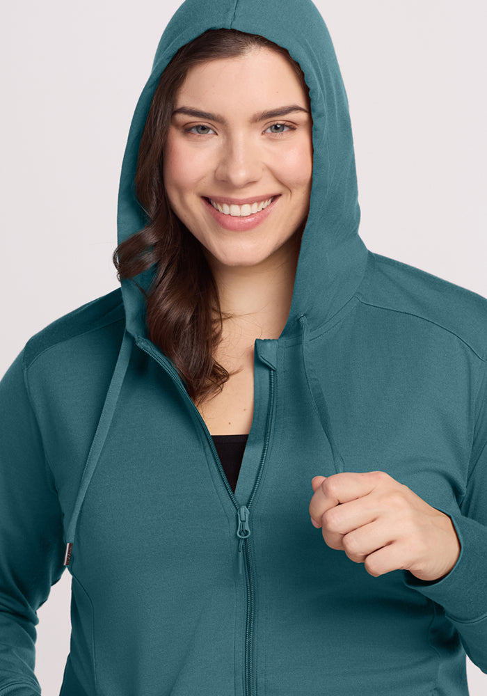 Woman with long brown hair smiles in the Woolx Ryann Hoodie • Final Sale - Tidepool, hood up and holding a drawstring.