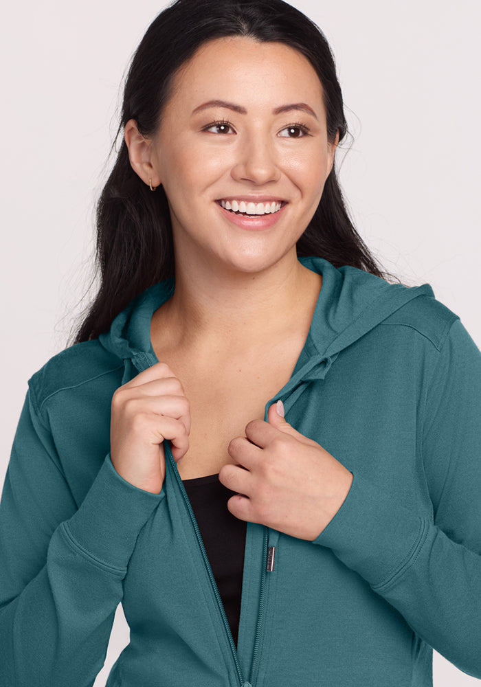 Smiling woman in the Woolx Ryann Hoodie • Final Sale - Tidepool, unzipped slightly, looking off to the side.