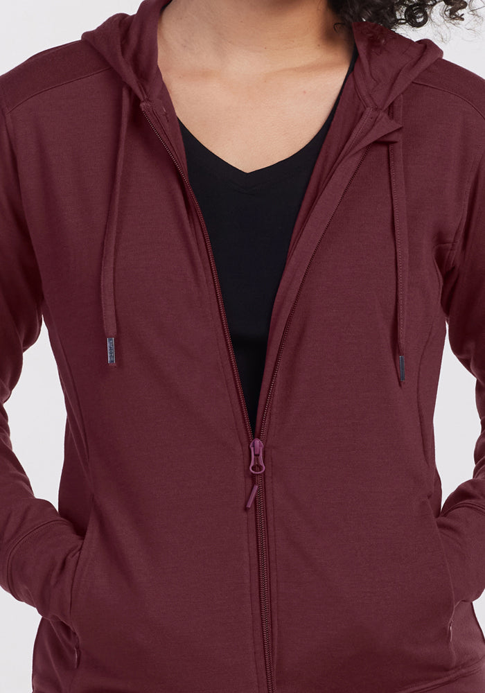 Someone wearing the Woolx Ryann Hoodie in Toasted Garnet over a black V-neck, hands in the hoodie’s pockets.