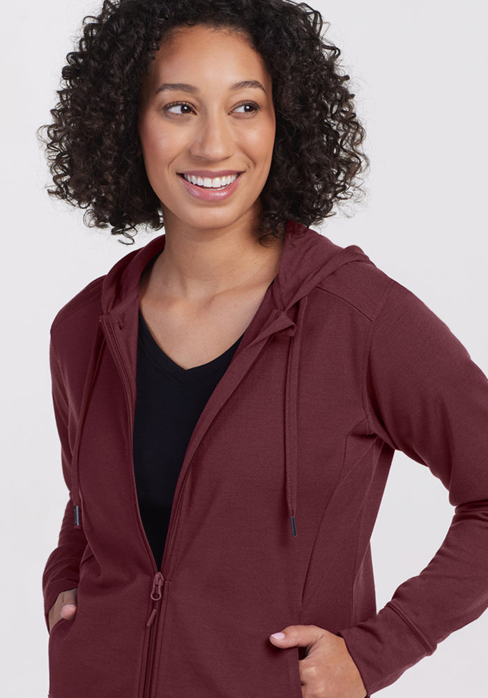 Smiling woman in Woolx Ryann Hoodie • Final Sale - Toasted Garnet, hands in pockets over a black top.