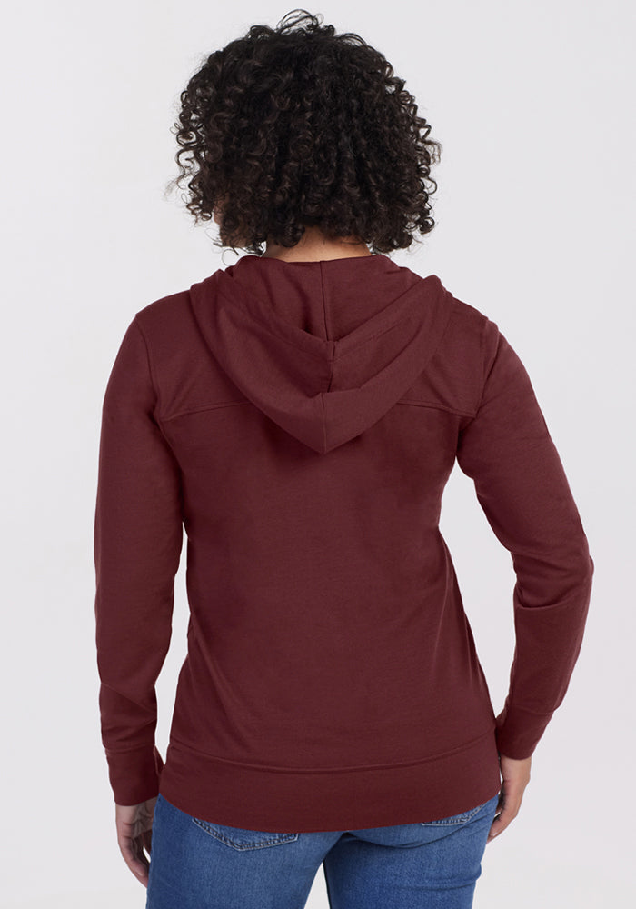 Person with curly hair wearing the Woolx Ryann Hoodie in Toasted Garnet and blue jeans, shown from the back.
