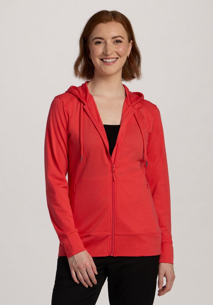 A smiling woman models the Woolx Ryann Hoodie in Hibiscus over a black top, standing against a plain light background. | Shea is 5’9”, wearing a size S