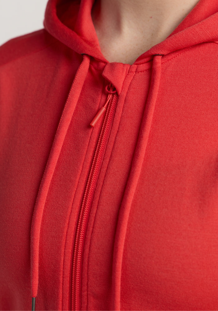 Close-up of a person wearing the Woolx Ryann Hoodie in Hibiscus, a red merino wool zip-up—ideal for travel.