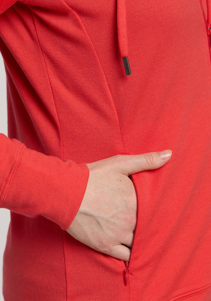 A hand rests in the pocket of the Woolx Ryann Hoodie - Hibiscus, a lightweight travel essential.