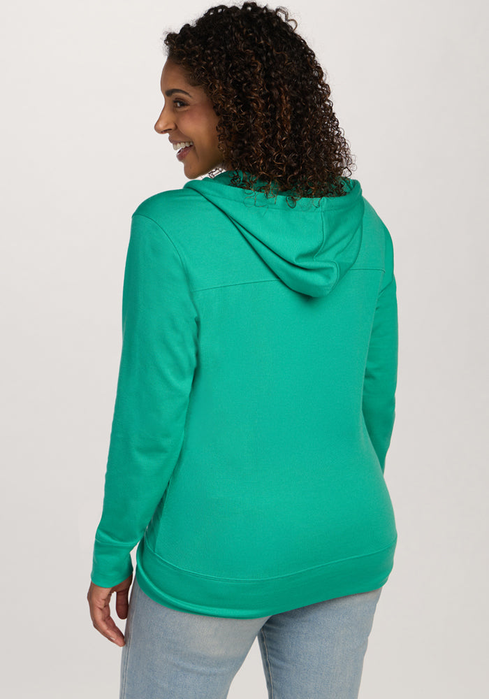 Smiling woman with curly hair in a Woolx Ryann Hoodie - Jungle and light jeans, facing away from the camera.