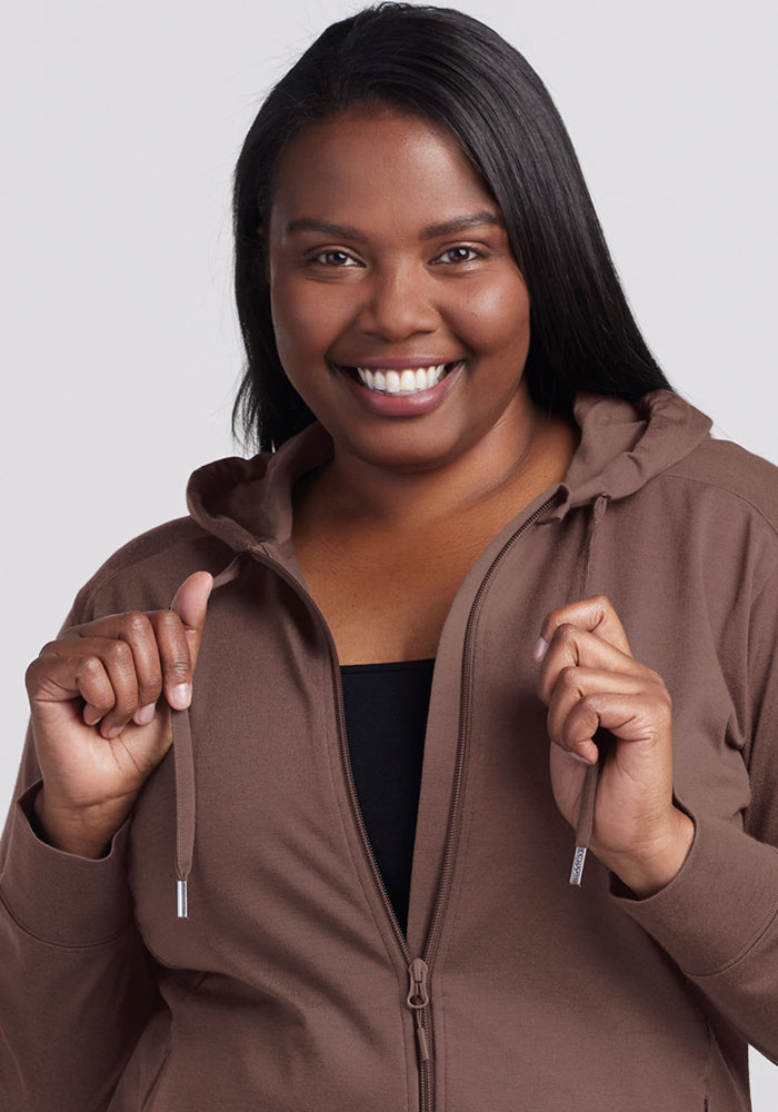 Smiling woman in a Woolx Ryann Hoodie - Peppercorn, holding strings, with straight dark hair against a plain background.