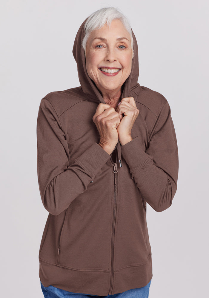 Smiling older woman in the Woolx Ryann Hoodie - Peppercorn, holding the hood—a cozy travel essential.