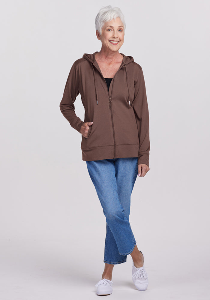 Smiling older woman in the Woolx Ryann Hoodie - Peppercorn, blue jeans, and white sneakers—a travel essential.