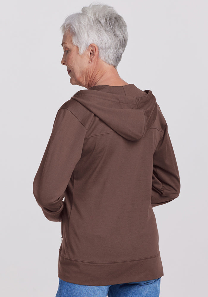 Older woman with short gray hair wears a Woolx Ryann Hoodie in Peppercorn and blue jeans, facing away; a travel essential.