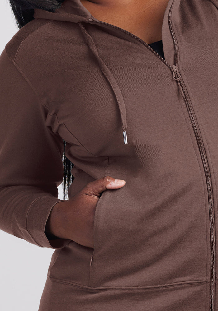 A person in a Woolx Ryann Hoodie - Peppercorn, travel essential, one hand in pocket, shown shoulders to hips.